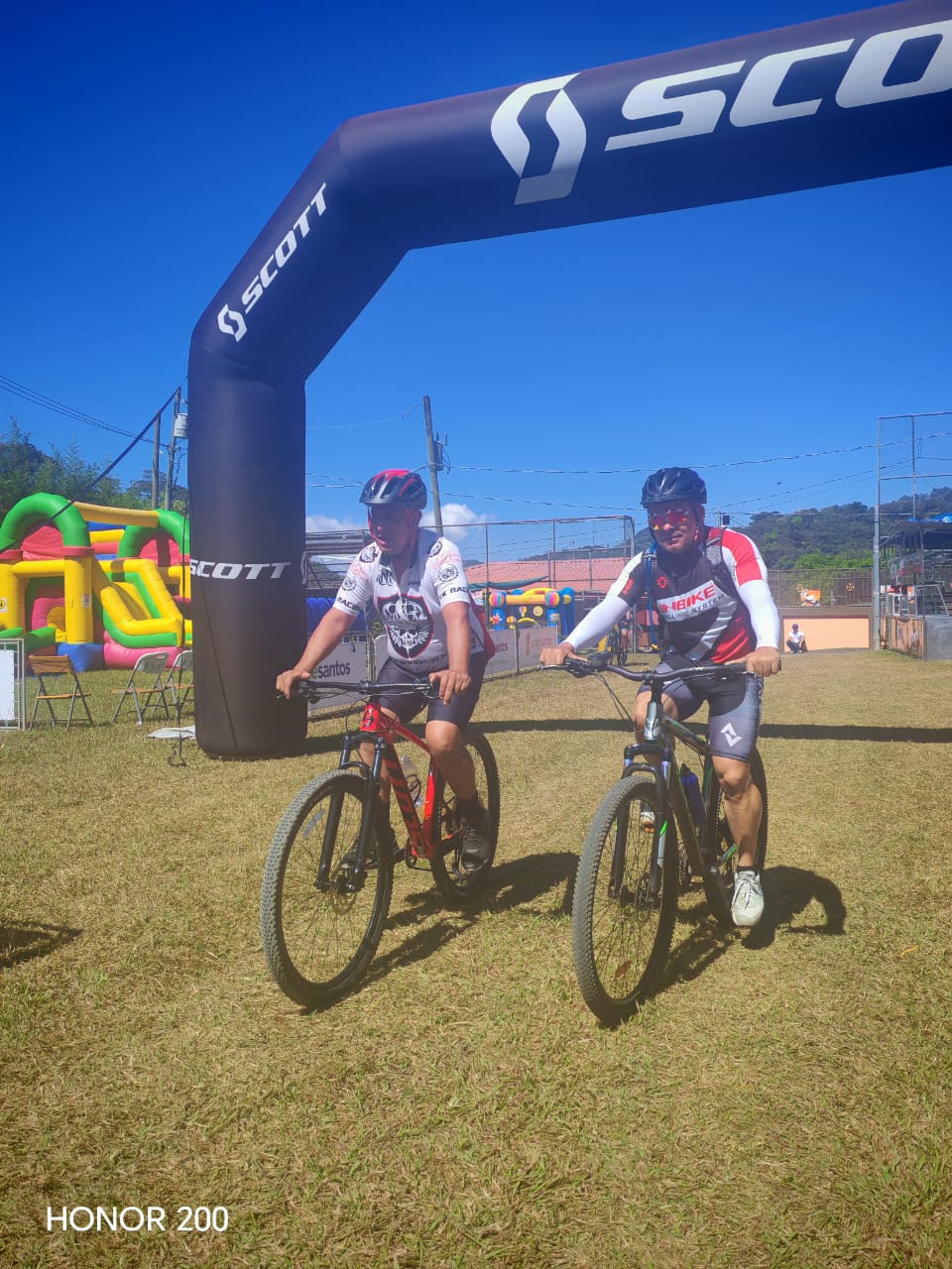 AcostaMTB — dos ciclistas bajo arco Scott